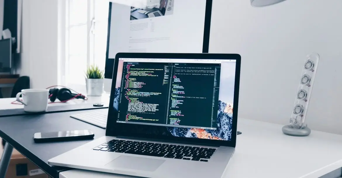 A MacBook with lines of code on its screen on a busy desk